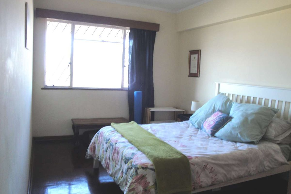 A standard bedroom featuring timber flooring and a window with security bars, offering a functional space with neutral wall finishes.