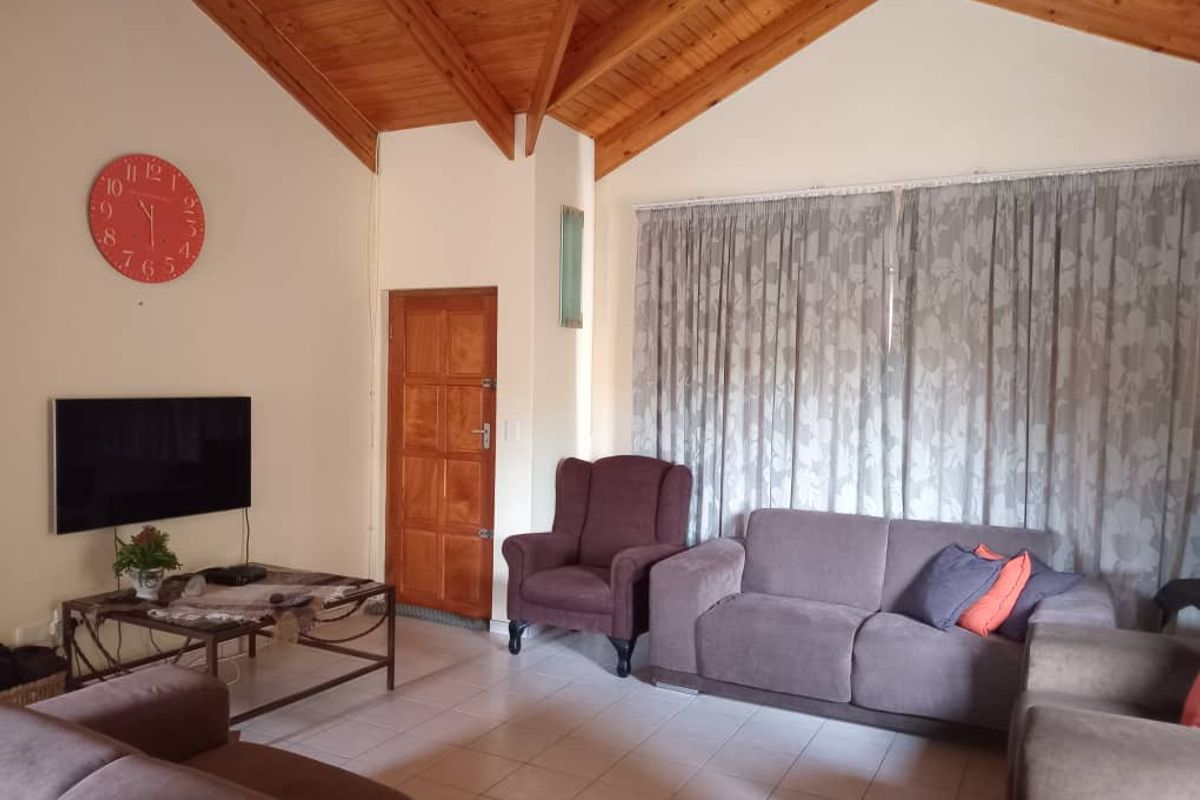 Spacious living room featuring high vaulted timber ceilings, tiled flooring, and large windows with curtains, creating a bright and airy atmosphere.