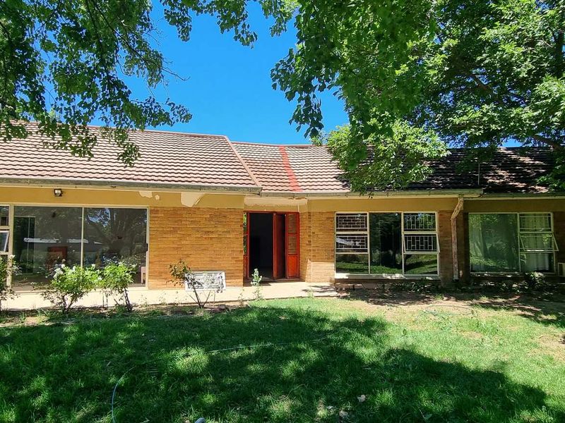 Rear view of a single-story brick house featuring a tiled roof, sliding glass doors, and a concrete patio area overlooking the garden.