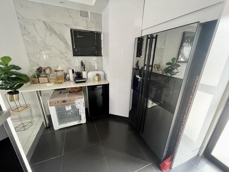 A modern scullery featuring marble-look wall tiling, sleek cabinetry, and dark floor tiles, providing a functional and stylish secondary kitchen or prep area.