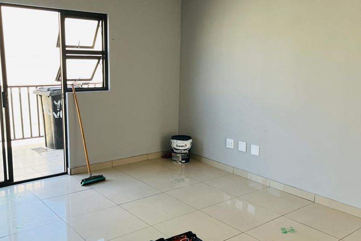 An empty, well-lit living area featuring neutral grey walls, polished floor tiles, and a sliding door providing access to an outdoor balcony.