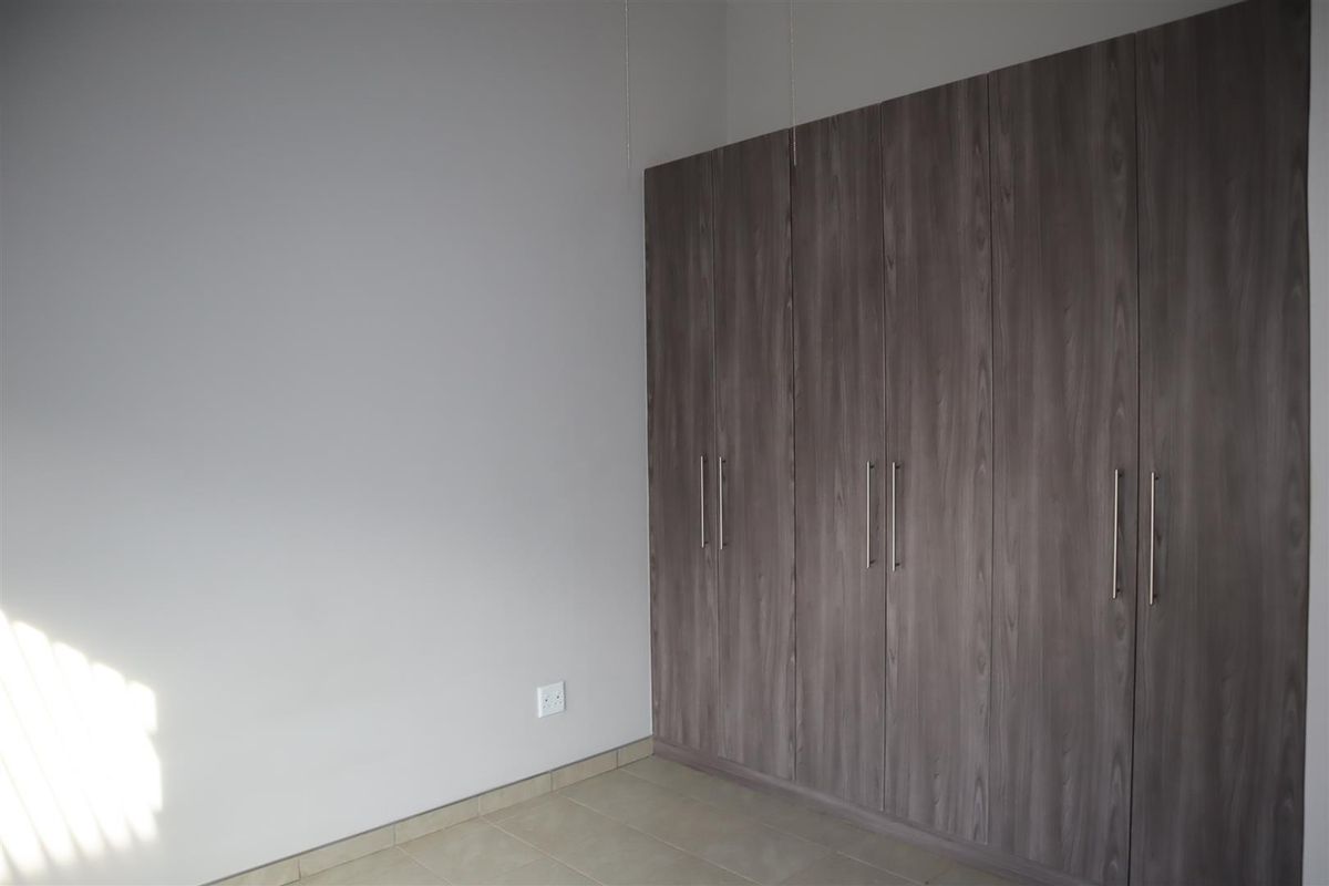 A clean, empty bedroom featuring modern wood-finish built-in cupboards and neutral tiled flooring.