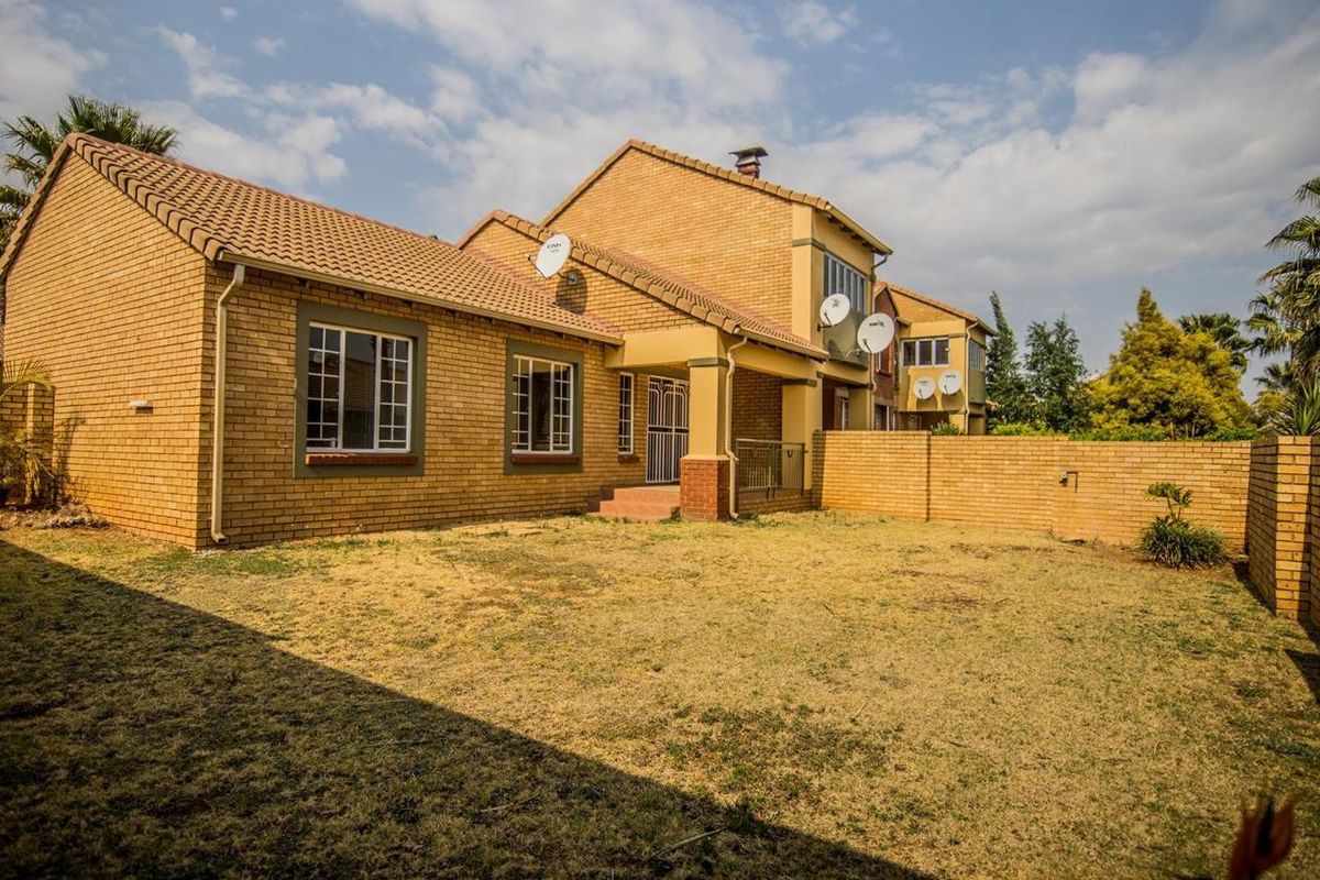 Rear view of a face brick townhouse featuring a private garden, covered patio area, and secure boundary walling.