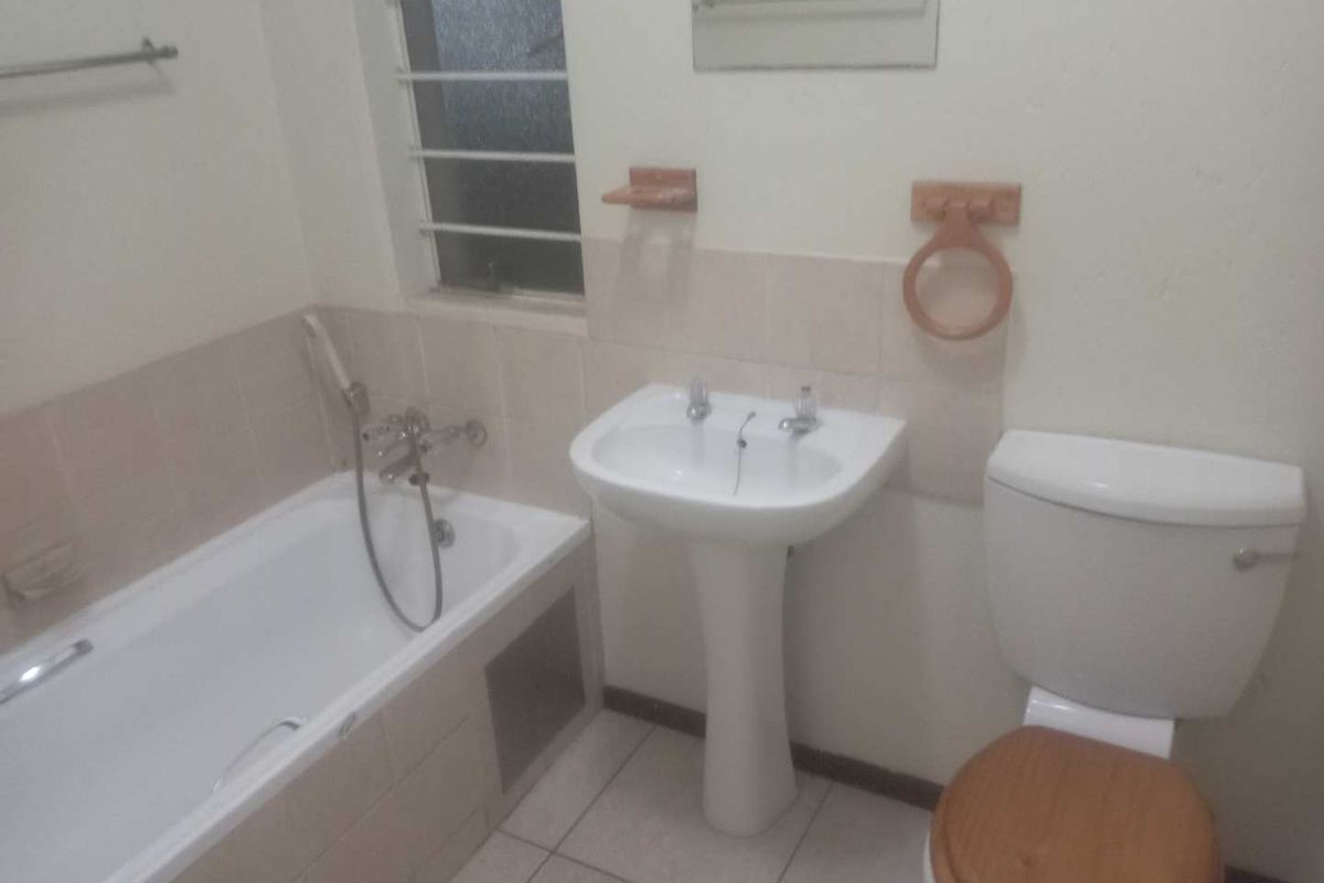 A functional bathroom featuring a standard bathtub with shower mixer, pedestal basin, and toilet, finished with neutral wall tiles.