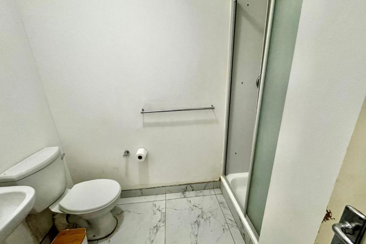 A compact bathroom featuring a shower enclosure, toilet, and marble-look floor tiles, presenting a functional space in need of minor cosmetic updates.