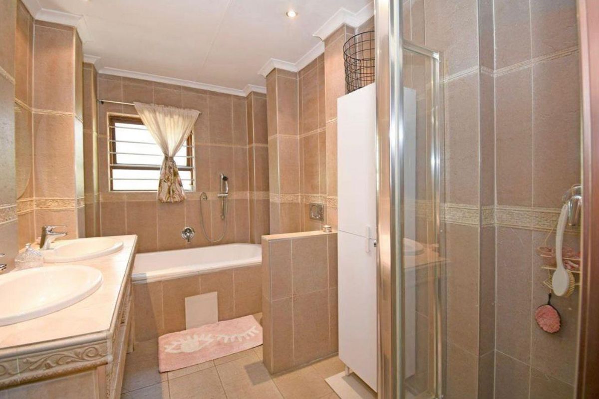A spacious bathroom featuring a double vanity, a built-in bathtub, and a separate glass-enclosed shower with neutral floor-to-ceiling tiling.