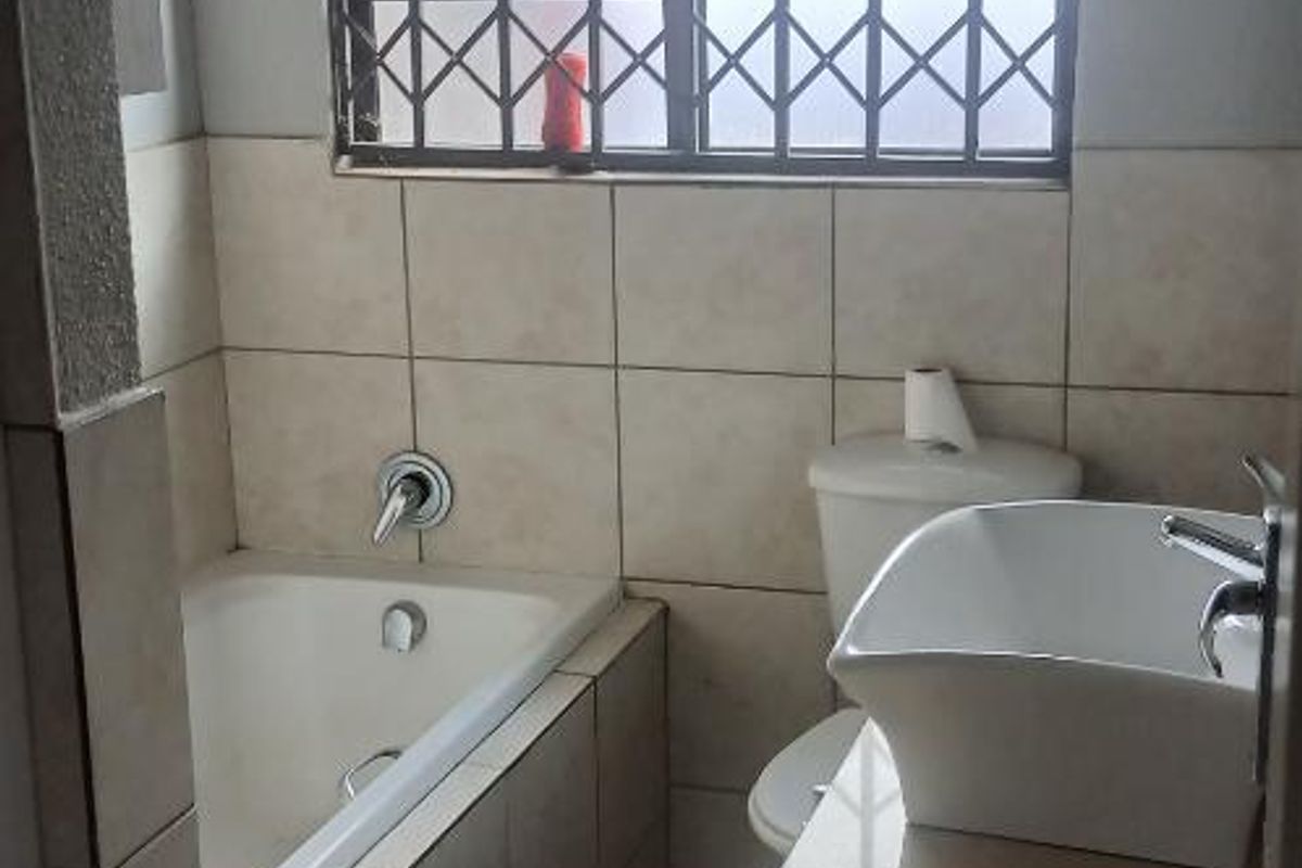 A functional bathroom featuring a built-in bathtub, a modern vessel sink vanity, and a window with security bars.