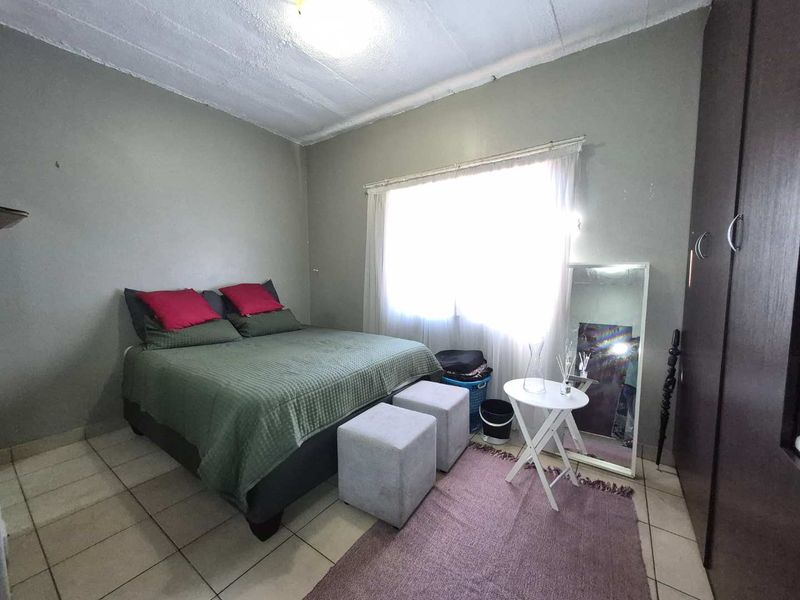 A functional bedroom featuring tiled flooring, a built-in wardrobe, and a window allowing natural light, providing a neutral base for personalization.