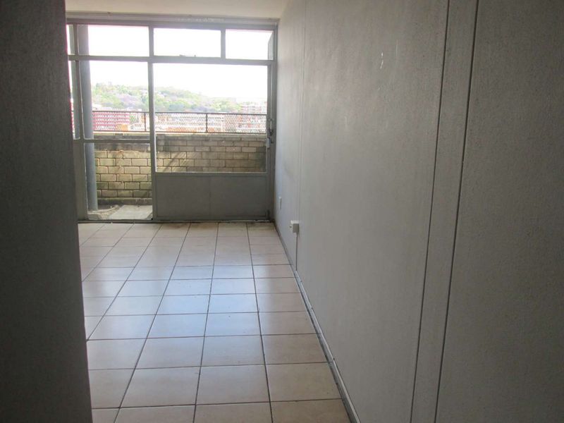 An empty living area featuring tiled flooring and a large sliding glass door leading to an outdoor balcony space.