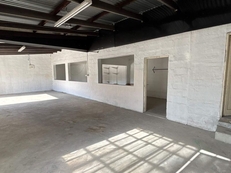 An open-plan industrial utility space featuring exposed corrugated metal ceilings, concrete flooring, and internal service windows, suitable for workshop or storage use.