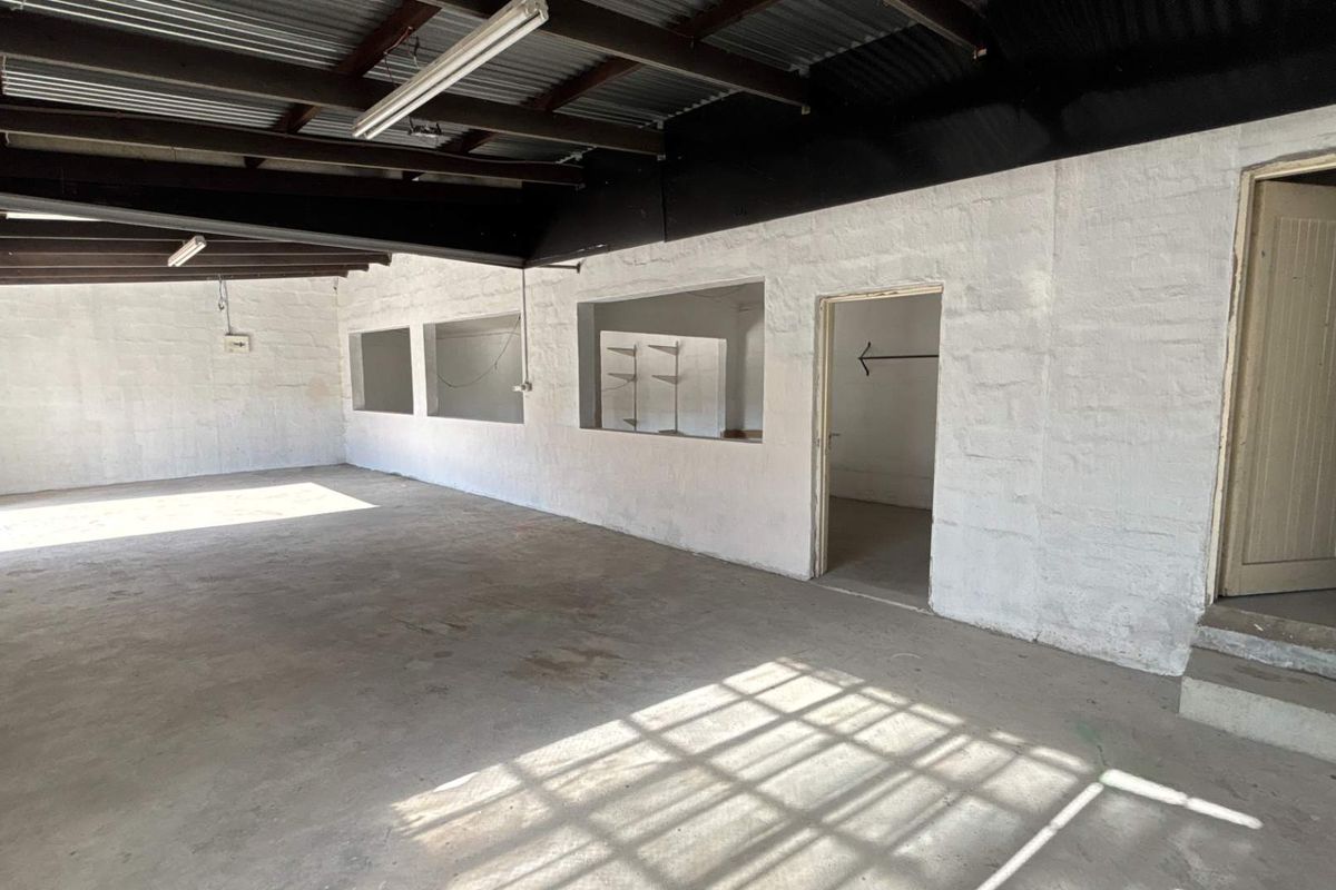 An open-plan industrial utility space featuring exposed corrugated metal ceilings, concrete flooring, and internal service windows, suitable for workshop or storage use.