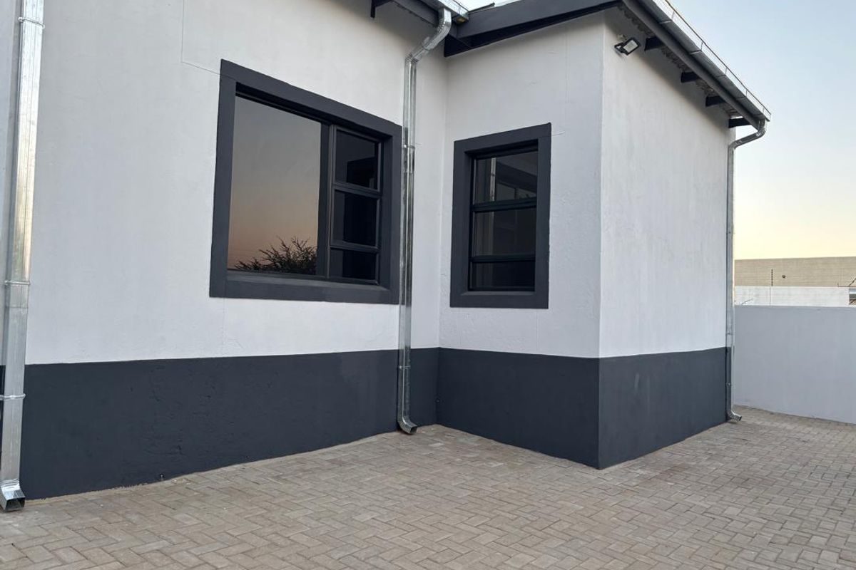A well-maintained rear exterior view featuring modern white and dark grey painted walls, aluminium window frames, and a clean paved courtyard area.