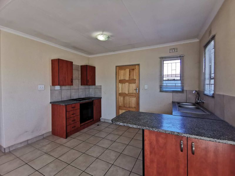 A functional kitchen featuring built-in wooden cabinetry, granite countertops, a built-in oven and hob, and tiled flooring.