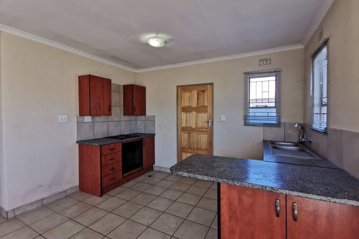 A functional kitchen featuring built-in wooden cabinetry, granite countertops, a built-in oven and hob, and tiled flooring.