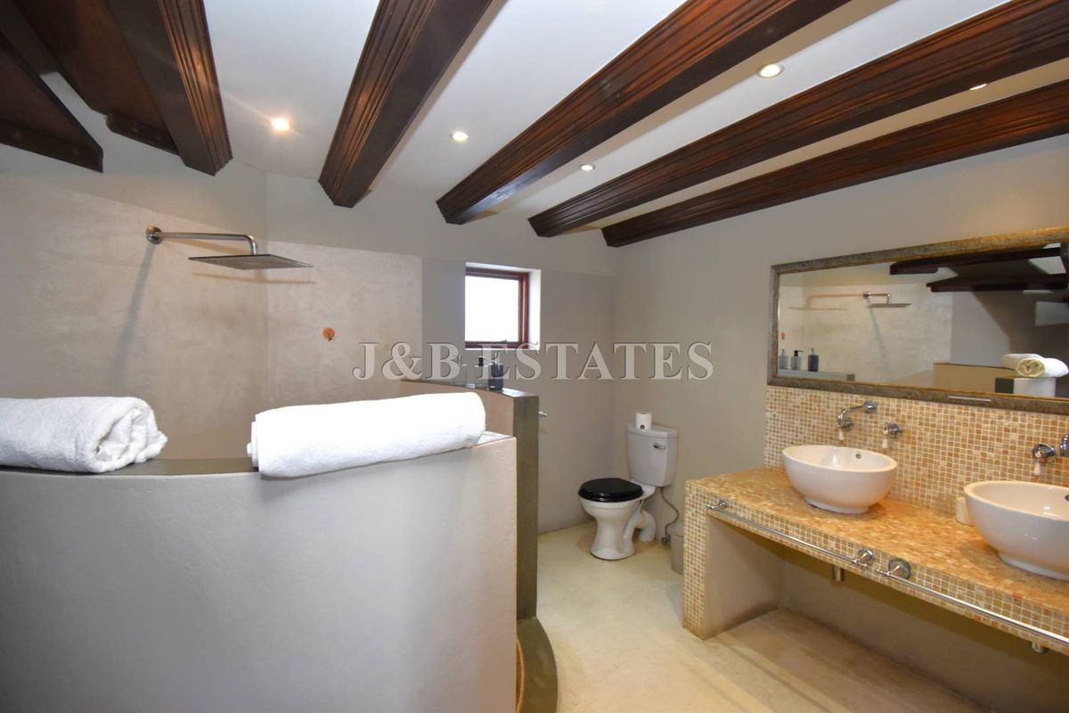A bathroom featuring a double vanity with mosaic tiling, a walk-in shower with a rainfall showerhead, and exposed timber ceiling beams.