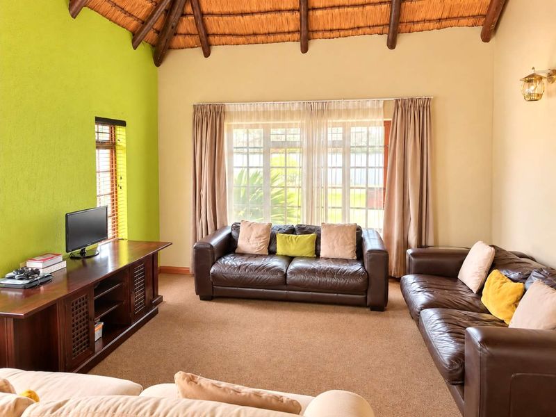 A spacious living room featuring a traditional thatched roof with exposed timber rafters, large windows, and a bright accent wall.