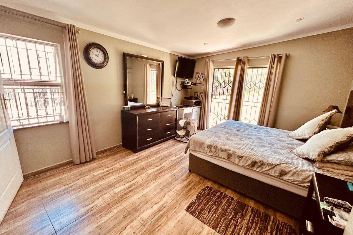 A spacious bedroom featuring wood-look tiled flooring, security bars on windows and doors, and neutral wall finishes.