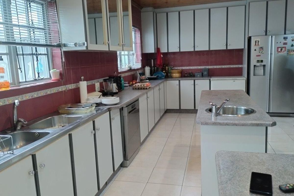 Spacious kitchen featuring extensive built-in cabinetry, a central island with a prep sink, tiled flooring, and a timber ceiling.