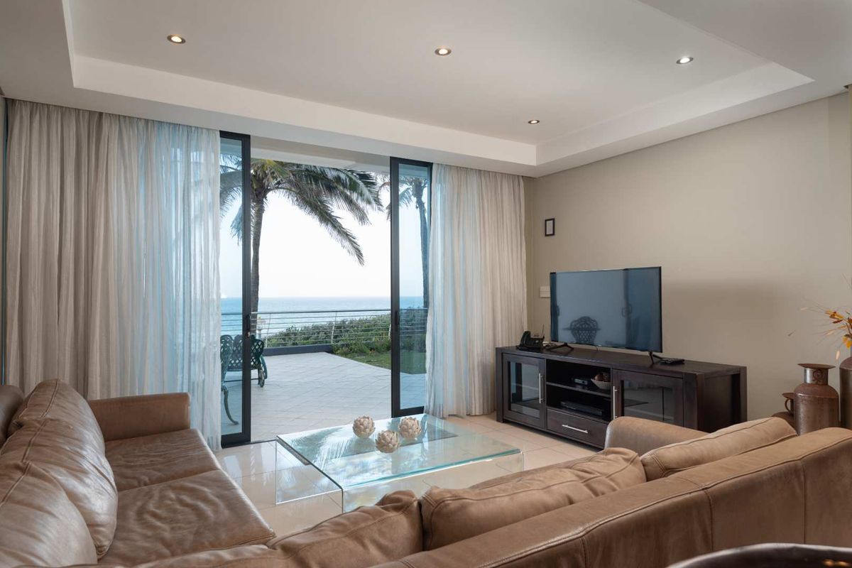 Spacious living room featuring tiled floors, recessed lighting, and large sliding glass doors opening to a balcony with ocean views.