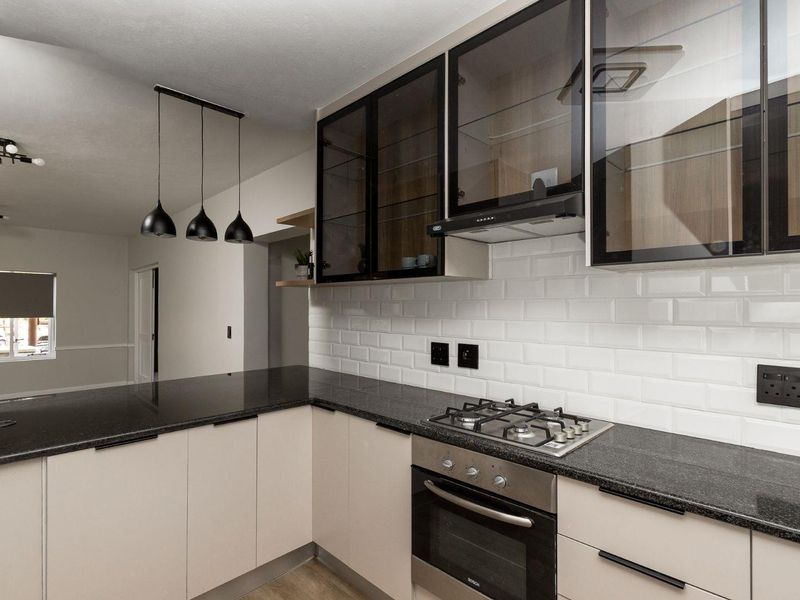 Modern kitchen featuring granite countertops, subway tile backsplash, gas hob, built-in oven, and sleek glass-front cabinetry with contemporary pendant lighting.