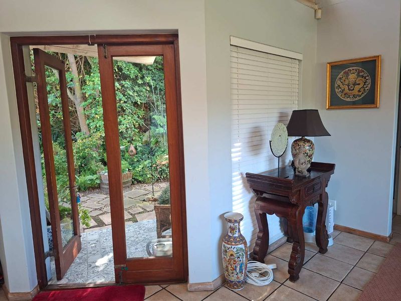 An entryway featuring timber-framed glass doors opening to a garden patio, with tiled flooring and neutral wall finishes.