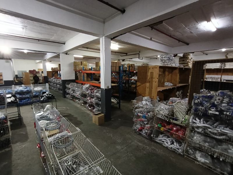 Industrial warehouse or storage space featuring concrete flooring, exposed structural columns, and overhead fluorescent lighting, suitable for commercial or industrial inventory management.