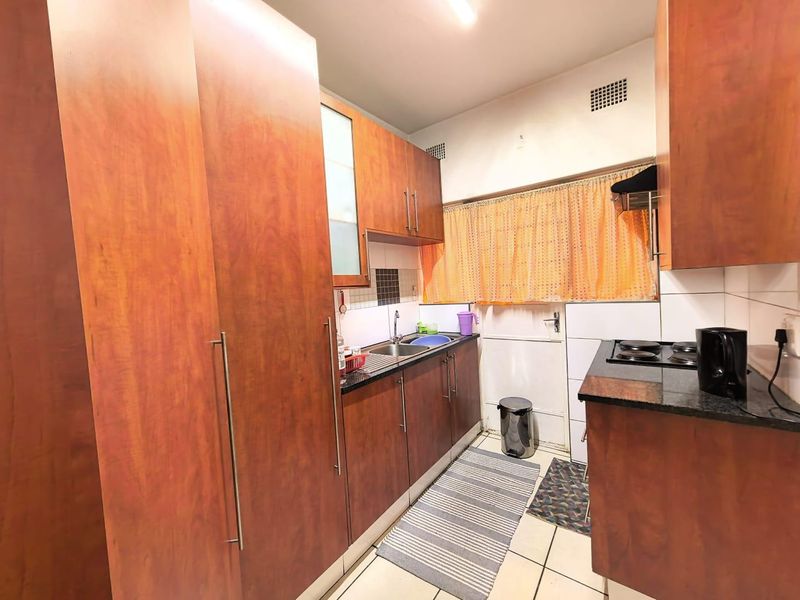 Compact kitchen featuring wood-look laminate cabinetry, granite countertops, a stainless steel sink, and an integrated electric hob with tiled backsplash.