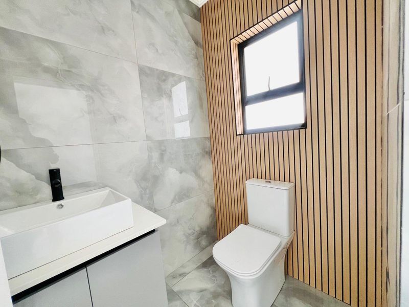 Modern bathroom featuring marble-look tiling, a sleek vanity with a vessel sink, and stylish slatted timber wall paneling.