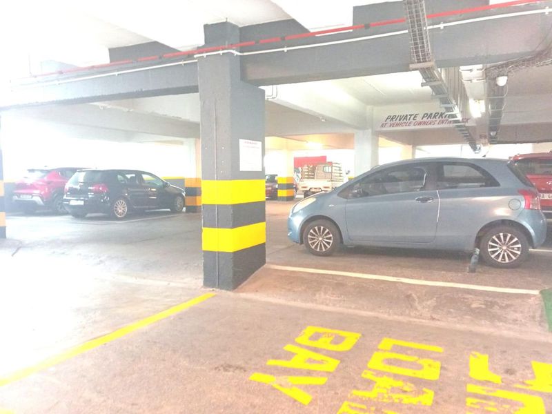 Covered parking garage area featuring concrete structural columns, overhead cable management systems, and designated parking bay markings.