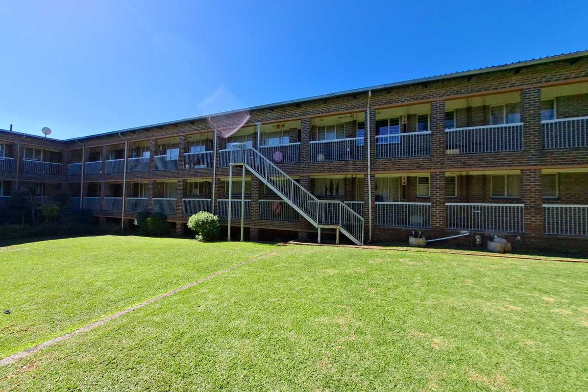 Rear view of a multi-story apartment building featuring brick exterior, communal balconies with metal railings, and an external staircase overlooking a shared lawn area.