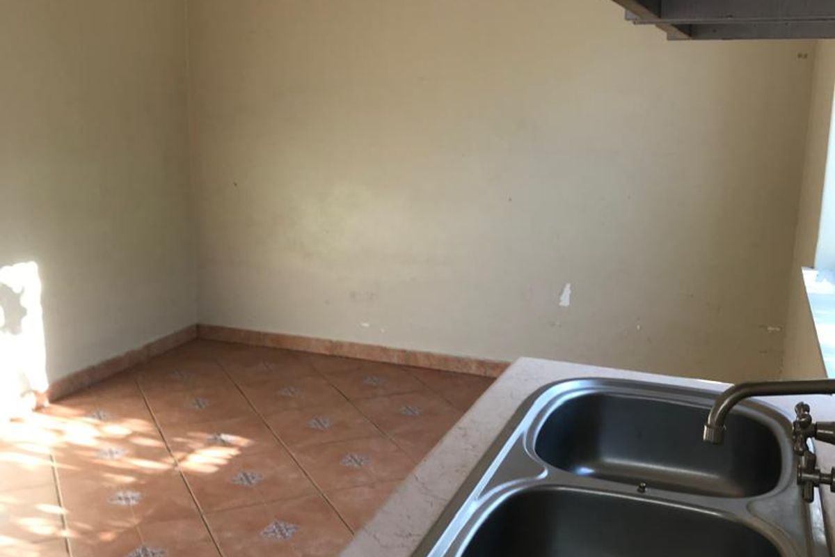 A functional kitchen area featuring a double stainless steel sink, tiled flooring, and neutral wall finishes, offering a blank canvas for potential updates.