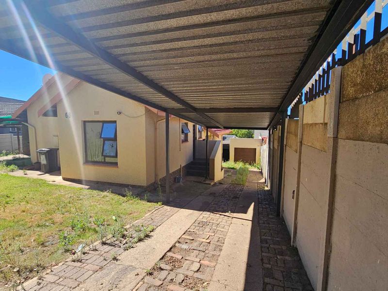 Front exterior view of the property featuring a covered carport, paved driveway, and a precast concrete boundary wall with an adjacent lawn area.