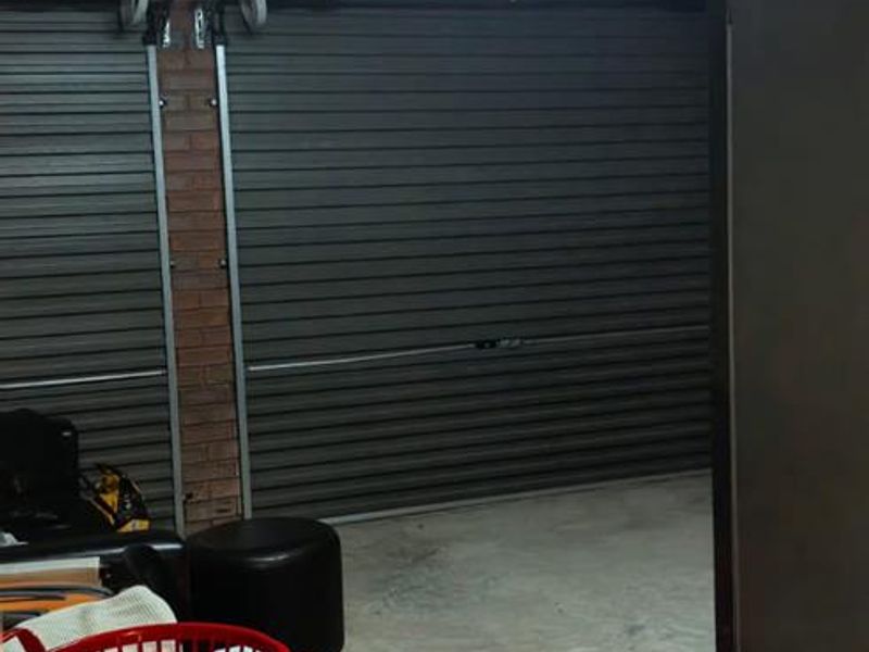 A functional garage space featuring a roll-up door, exposed brick walls, and overhead fluorescent lighting.