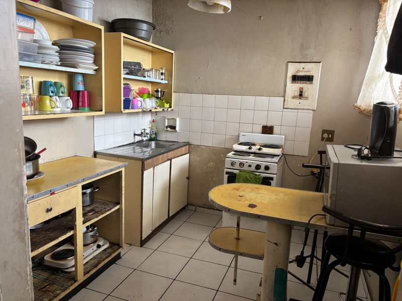 A dated kitchen featuring original cabinetry, a freestanding stove, tiled splashback, and ceramic flooring, requiring significant renovation and cosmetic updates.