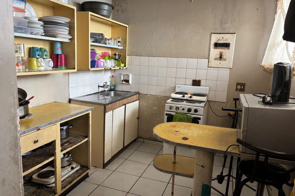 A dated kitchen featuring original cabinetry, a freestanding stove, tiled splashback, and ceramic flooring, requiring significant renovation and cosmetic updates.