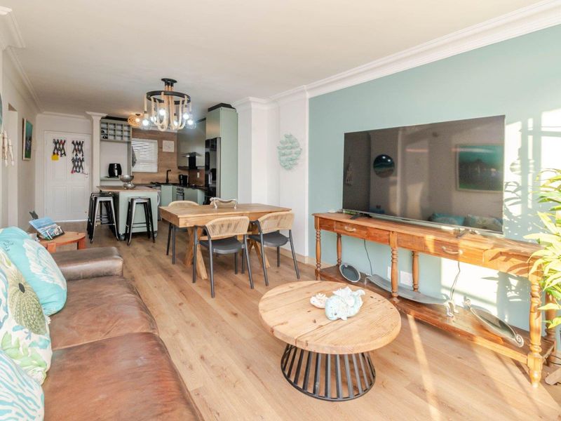 An open-plan living and kitchen area featuring light wood-look flooring, modern cabinetry, a central kitchen island, and crown molding throughout the space.