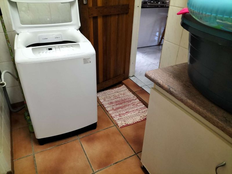 A functional laundry area featuring tiled flooring, built-in cabinetry with a stone countertop, and space for a top-loading washing machine.