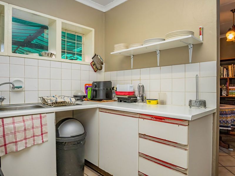 A functional kitchen area featuring laminate countertops, a double bowl sink, tiled splashbacks, and built-in cabinetry with visible signs of wear.