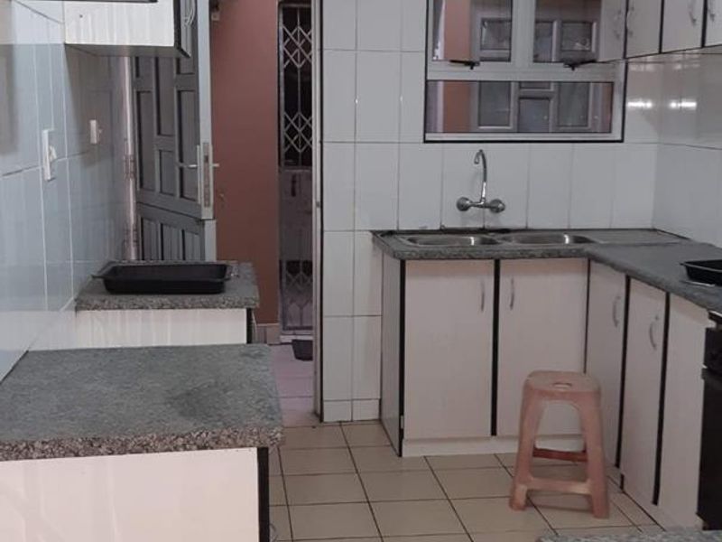 A functional kitchen featuring white built-in cabinetry, granite countertops, a double basin sink, and tiled flooring with direct access to an adjacent utility area.