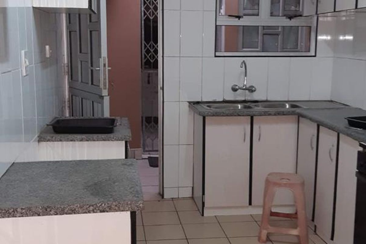 A functional kitchen featuring white built-in cabinetry, granite countertops, a double basin sink, and tiled flooring with direct access to an adjacent utility area.