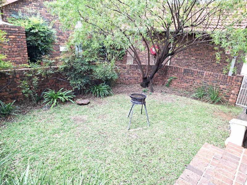 A private rear garden featuring a lawn, mature tree, and face brick boundary walls, accessible from a brick-paved patio area.