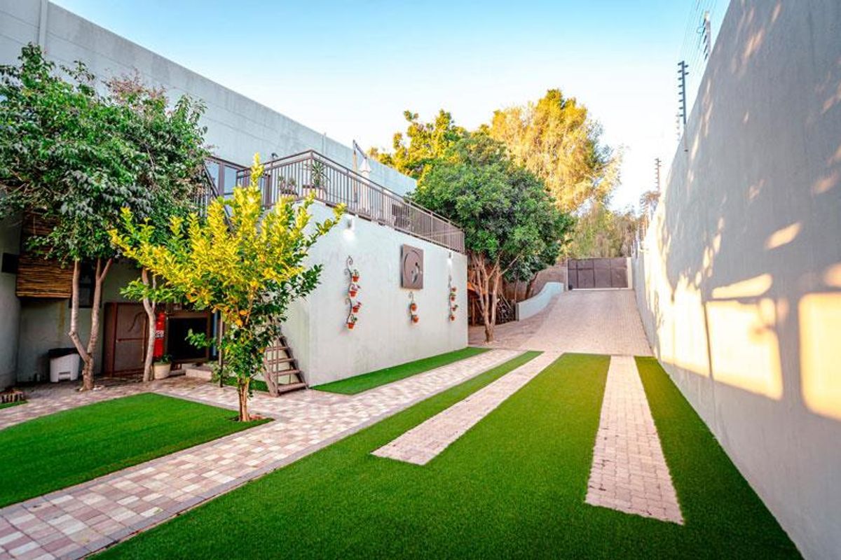 A well-maintained rear exterior area featuring a paved driveway, artificial lawn, and an elevated balcony with secure railing and electric fencing.