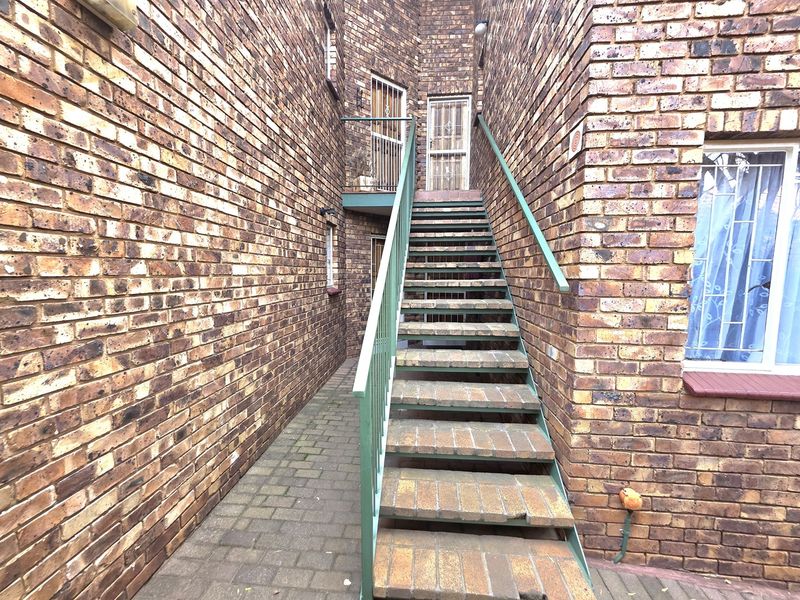 Exterior view of an apartment building featuring a brick facade, a metal staircase leading to upper levels, and paved ground area.