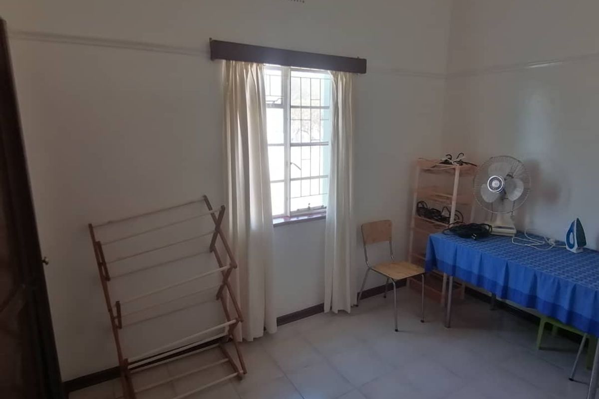 A simple bedroom featuring tiled flooring, a window with security bars, and a picture rail.