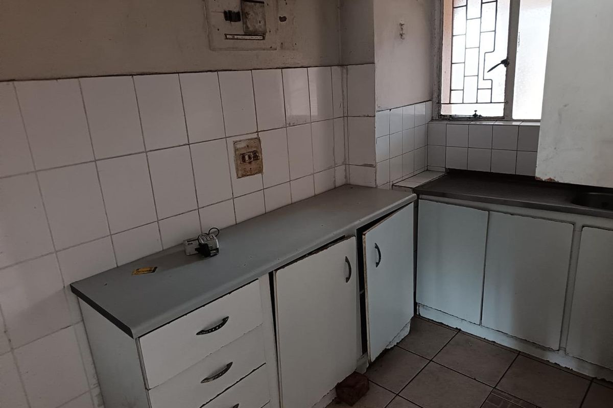A dated kitchen featuring built-in cabinetry, tiled splashbacks, and security bars on the window, requiring significant renovation to modernize the space.