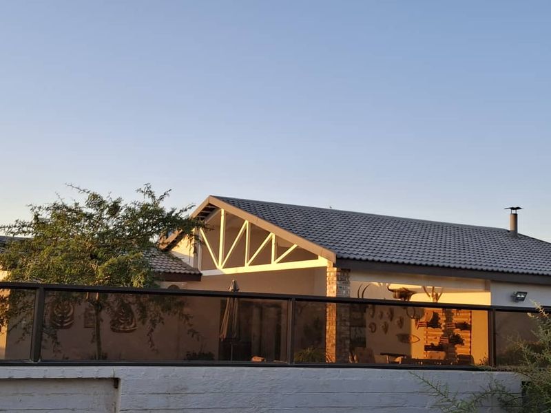 A covered patio area featuring exposed roof trusses, a brick support pillar, and a modern glass balustrade, overlooking the garden area.