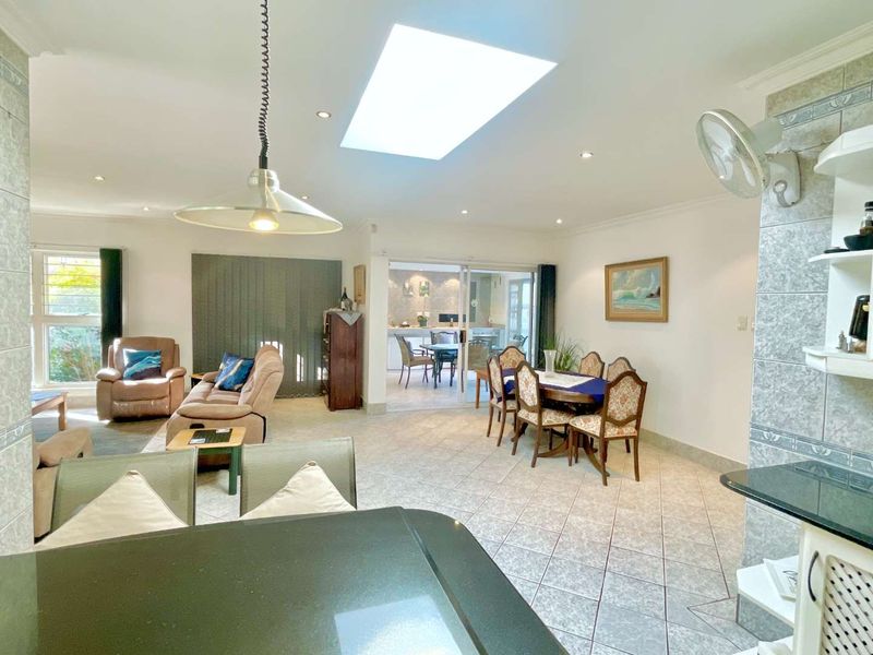 Spacious open-plan living and dining area featuring tiled flooring, a large skylight, and direct access to an adjacent patio through sliding glass doors.