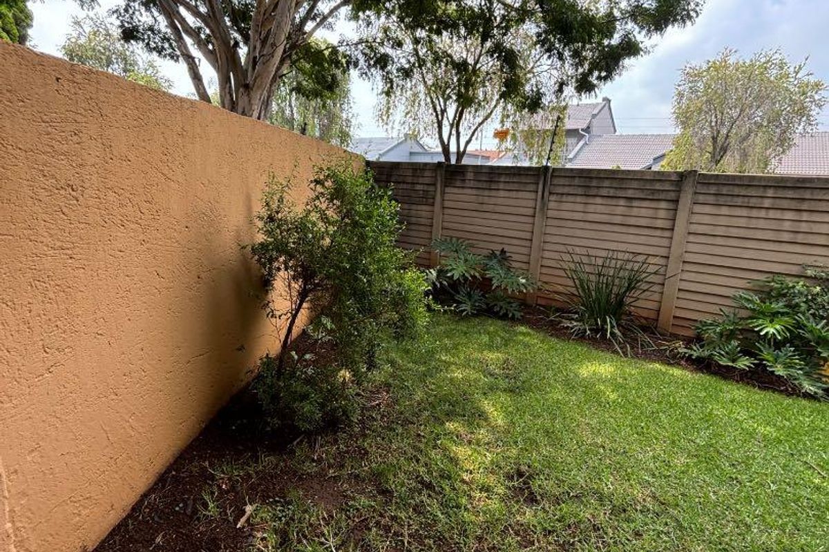 A private rear garden featuring a small lawn, paved patio section, and enclosed by a combination of rendered masonry and precast concrete boundary walls.
