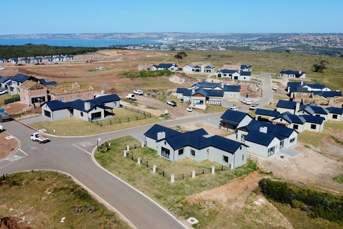 Aerial view of a developing residential estate featuring modern homes with dark pitched roofs, paved roads, and surrounding coastal landscape.