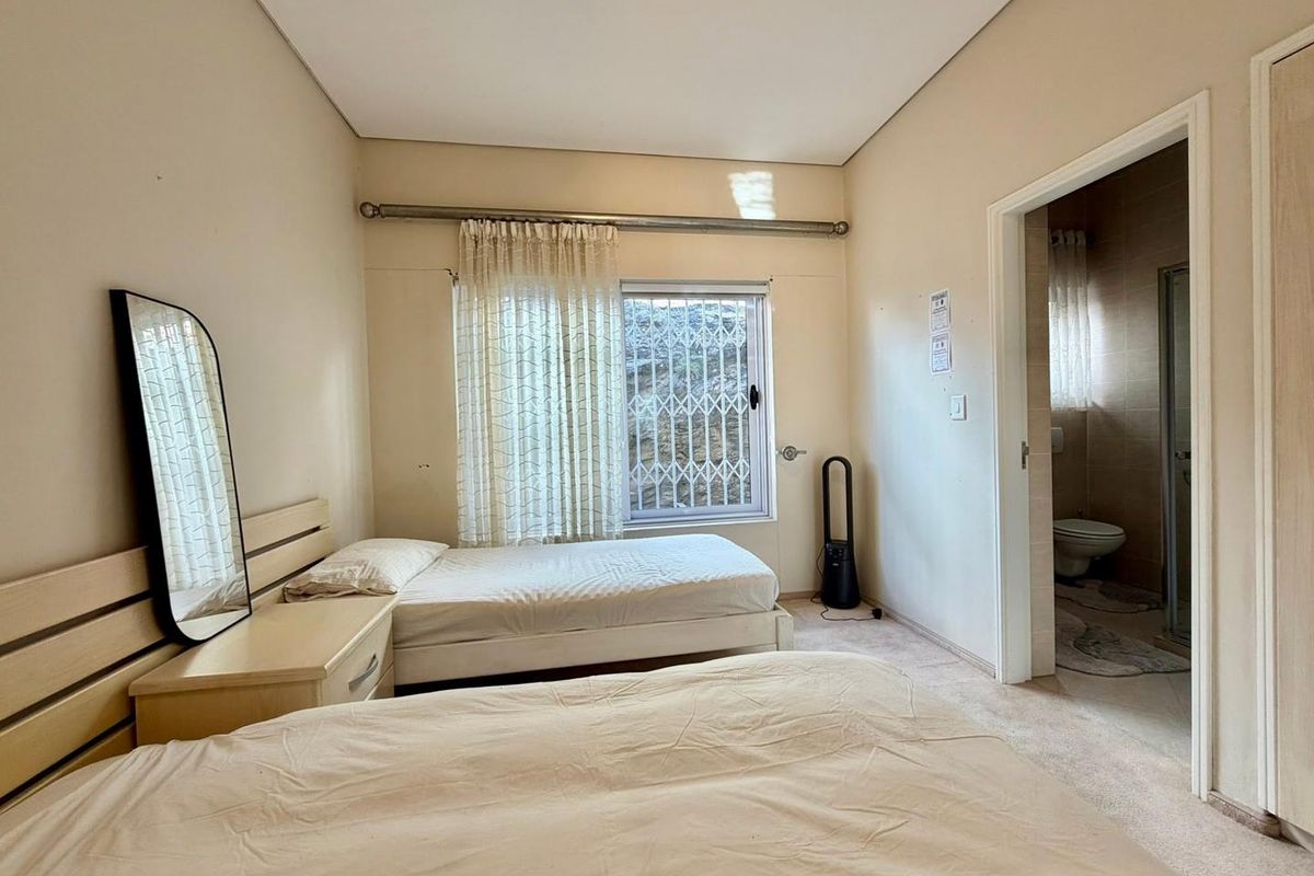 A functional bedroom featuring carpeted flooring, a window with security bars, and an adjoining en-suite bathroom.